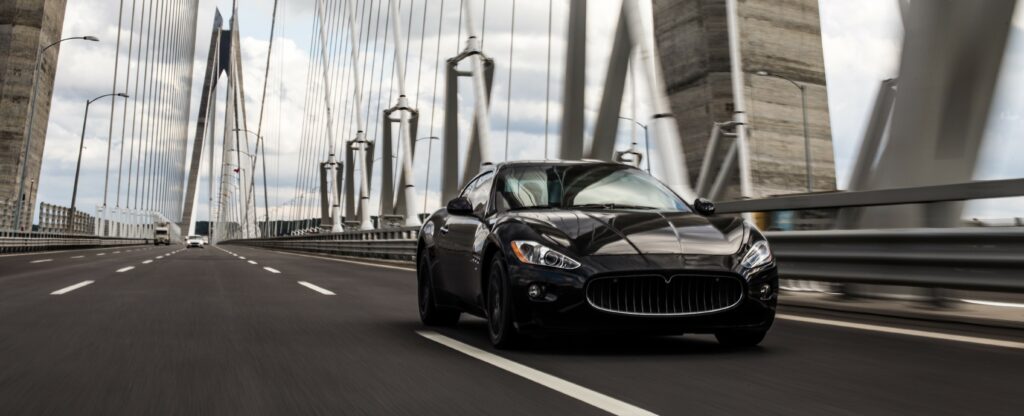 A black luxury car drives over a bridge.
