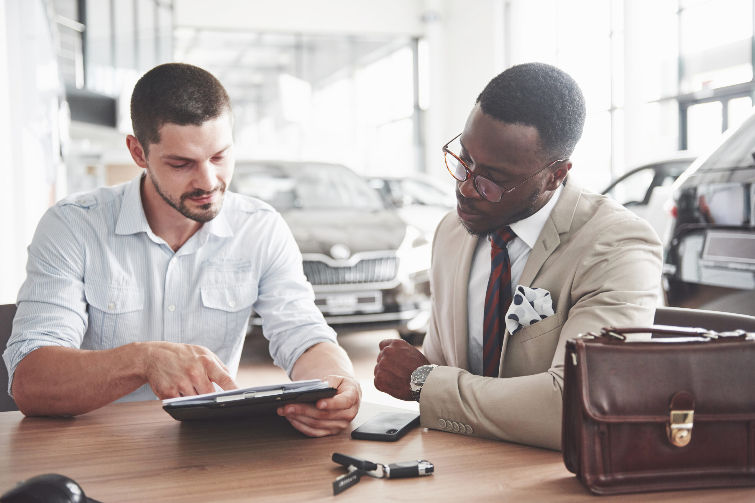 A man discusses the contract with a salesman at a luxury car dealership.