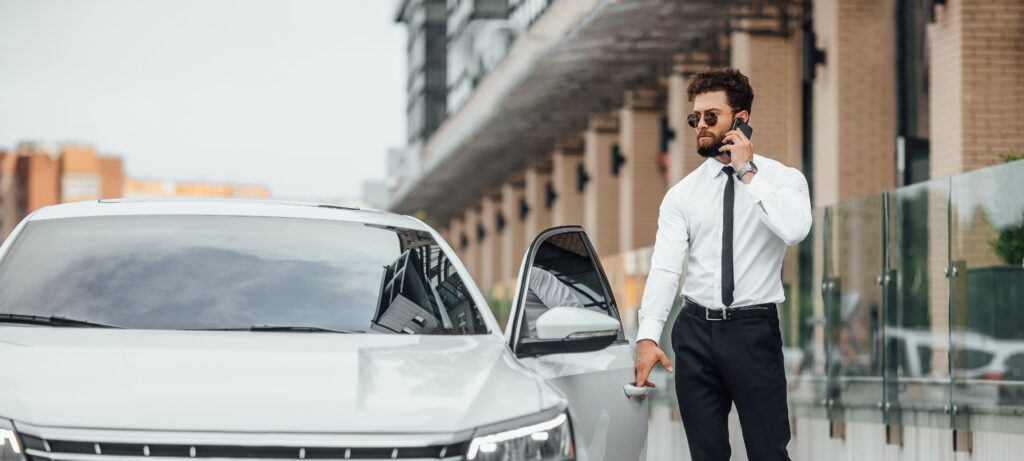 A businessman leans on his luxury car while on the phone.