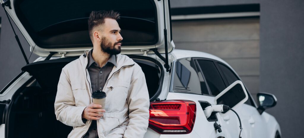 A middle-aged man charges his luxury electric car while drinking a coffee.
